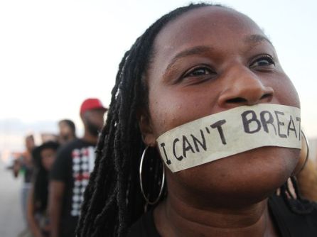 A Black woman with tape over her mouth on which the words "I can't breathe" are written